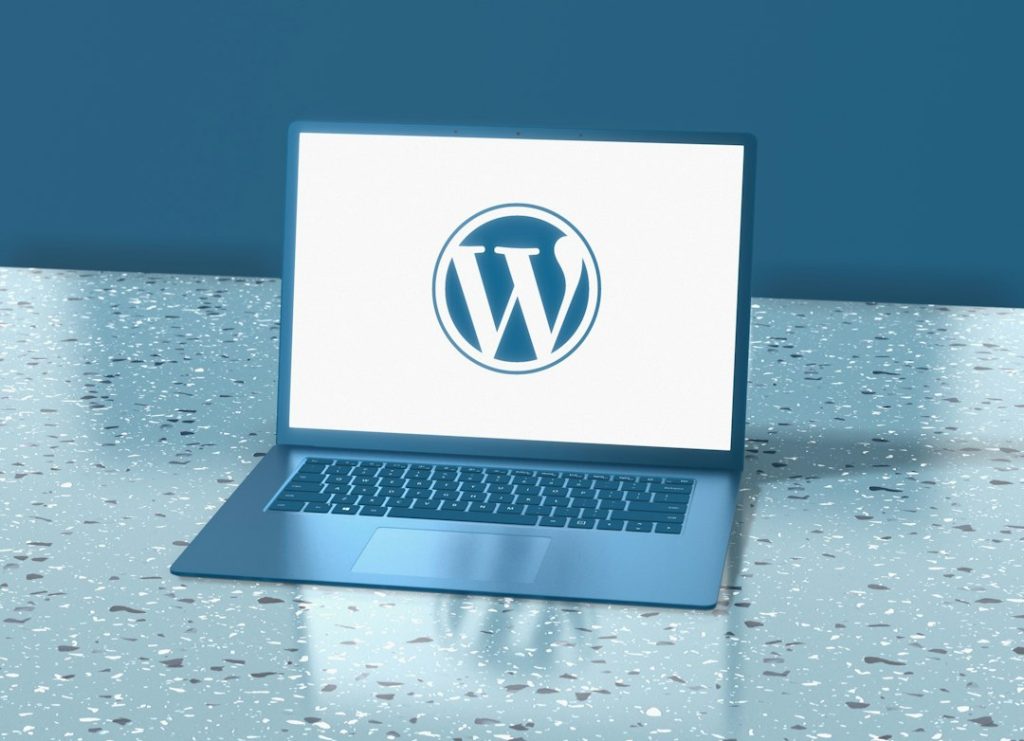 A blue laptop displaying the WordPress logo on a speckled blue surface wordpress error screen, bug icon, magnifying glass