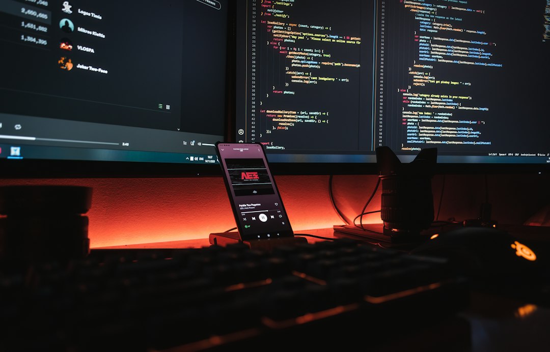 A smartphone displaying music on a desk with computer monitors showing code developer code smart contract testing